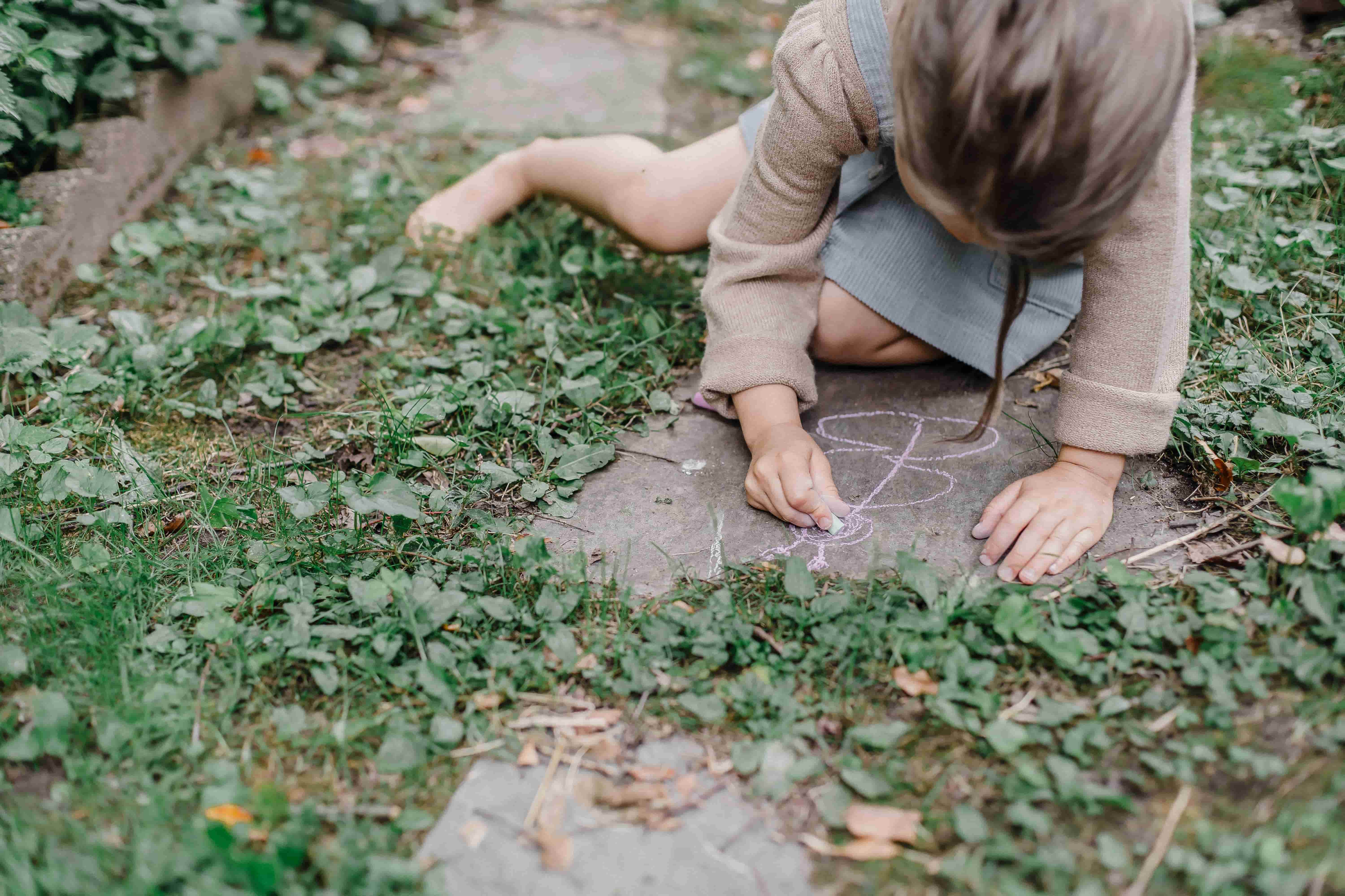 A young girl drawing with chalk on a rock outdoors, calmly focused on her artwork as part of a creative and expressive activity.