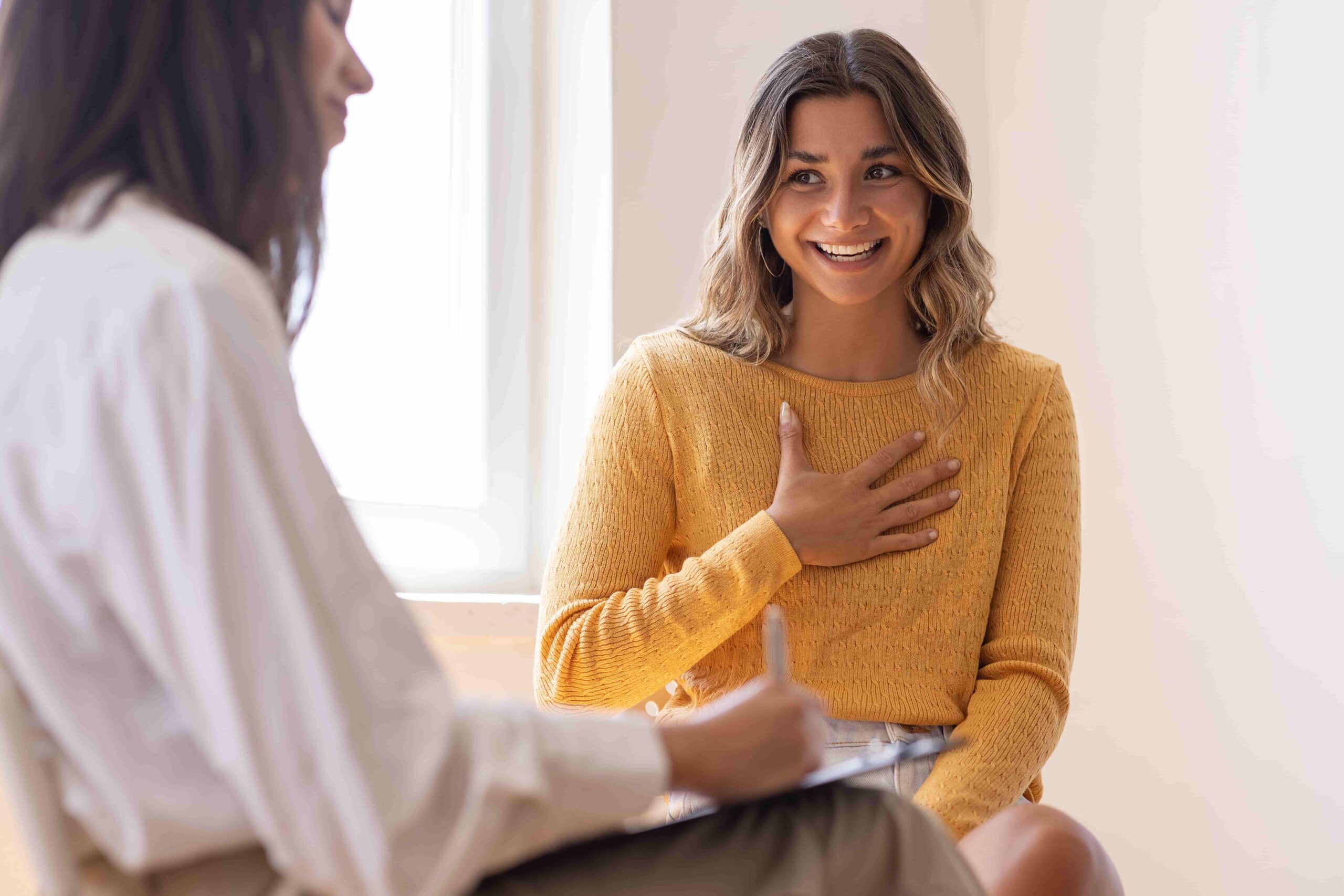 A woman smiles warmly while talking with a therapist during a counseling session in a bright room.